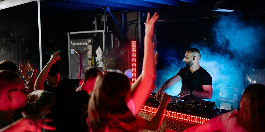 People dancing while raising their hands in the nightclub with the DJ playing music