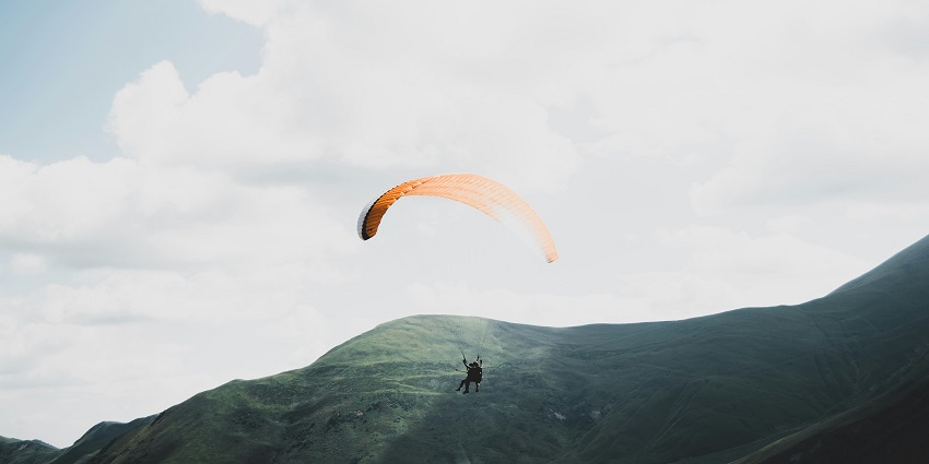 A person paragliding in Gurgaon amidst hilly terrains and misty weather in Sohna