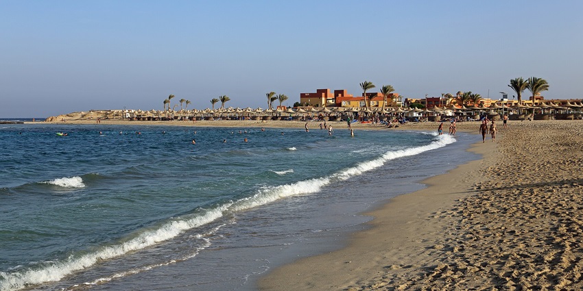 People are walking and enjoying their day on the sandy beach near a large water body.
