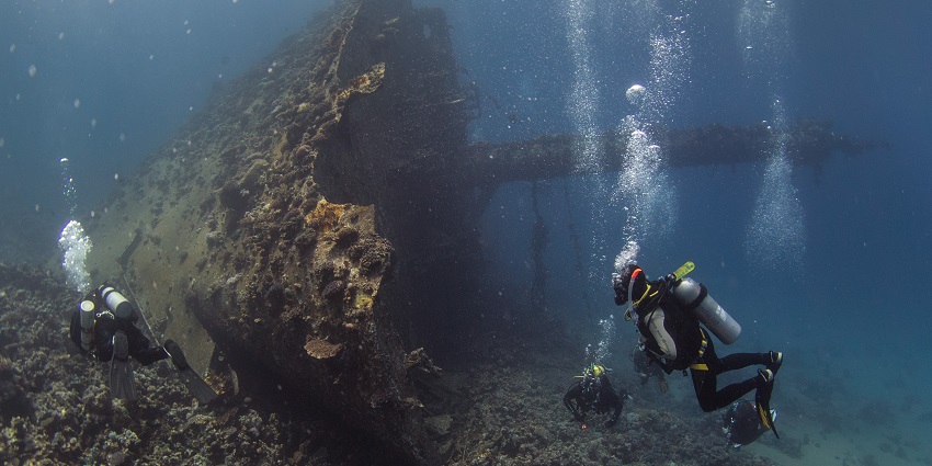 Multiple scuba divers with oxygen cylinders on their backs exploring the Abu Nuhas wrecks