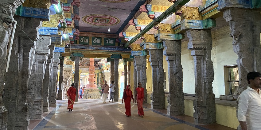 Interior of Adi Kumbeswarar temple with detailed pillars, ceiling and devotees visiting