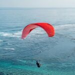 An image of a man enjoying paragliding adventure over the sea with clear blue water