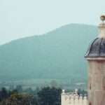 An image of a tower from the 19th century has a domed rooftop and can be seen from a hill.