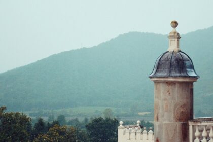 An image of a tower from the 19th century has a domed rooftop and can be seen from a hill.