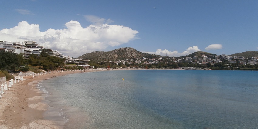 Image of picturesque Vouliagmeni beach surrounded by town and nature under blue sky