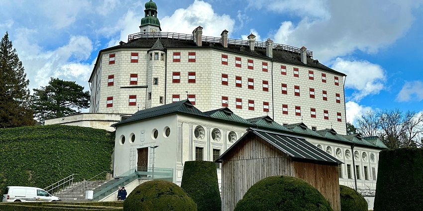 An image of the Ambras Castle, surrounded by lush gardens with panoramic views of the Alps