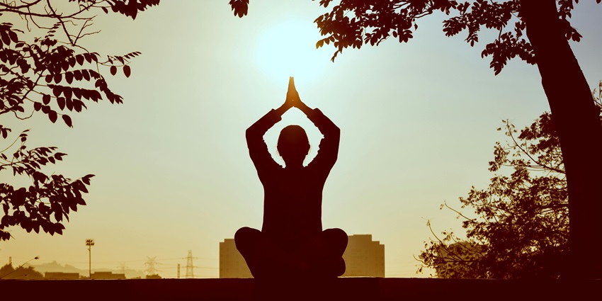 A girl is holding a yoga pose in front of a serene lake, facing the setting sun.