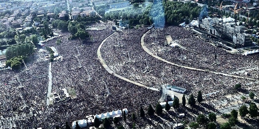 An aerial view shows a sea of people gathered for an energetic music concert.