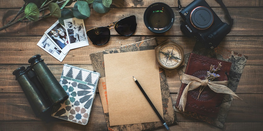 An image of travel things - a camera, pair of binoculars, a dairy, compass and more.