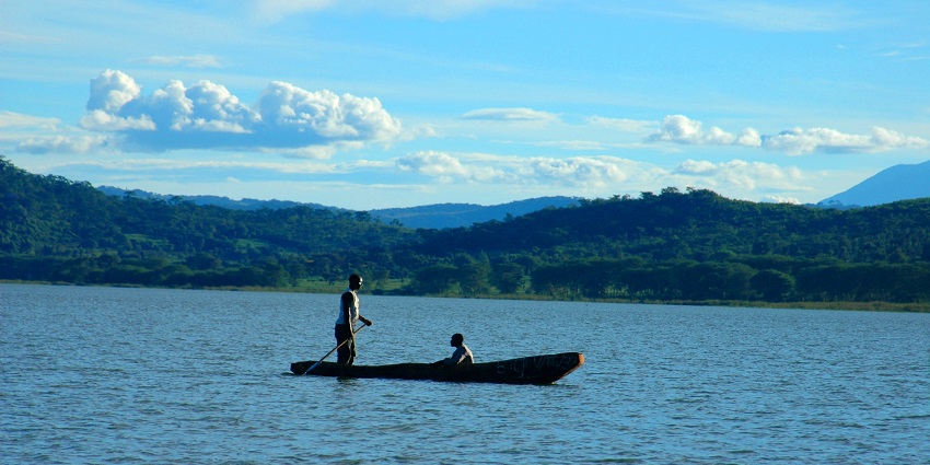 Two people canoeing on a boat in Lake Babati with small hills in the background.