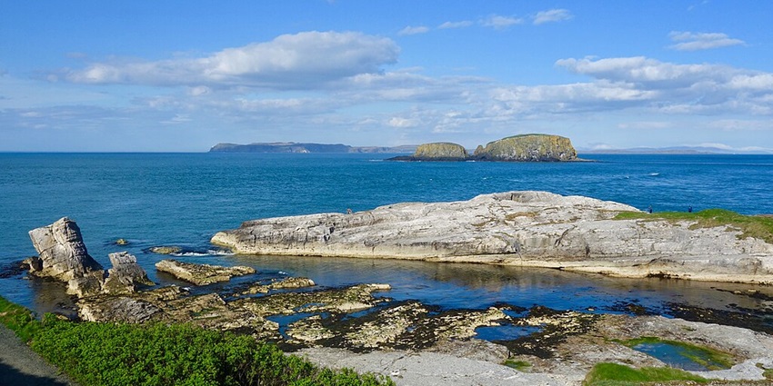 An Image of the Ballintoy Harbor with stone structures, green grass, and a boat.