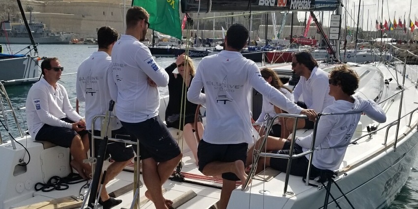 Sailors in white uniform sitting in a boat getting ready for the Rolex Middle Sea Race.