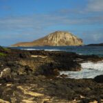 Picture-perfect beach with hilly areas, with waves crashing on the black rocky shore