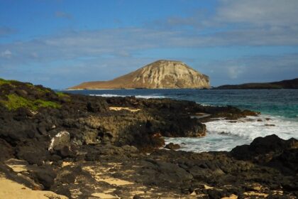 Picture-perfect beach with hilly areas, with waves crashing on the black rocky shore