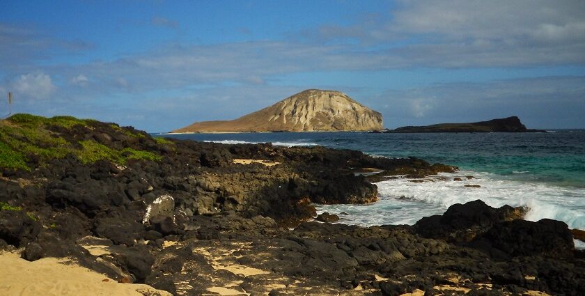 Picture-perfect beach with hilly areas, with waves crashing on the black rocky shore