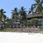 A pristine beach in Kenya with warm white sand, several palm trees and a resort nearby