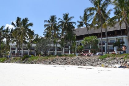 A pristine beach in Kenya with warm white sand, several palm trees and a resort nearby