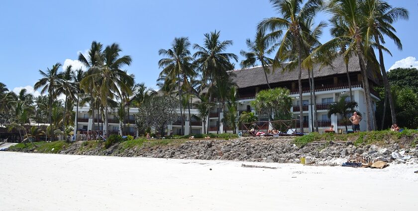 A pristine beach in Kenya with warm white sand, several palm trees and a resort nearby