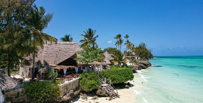 A beautiful beach with white sand, trees, beach chairs, and clear water surrounding it.