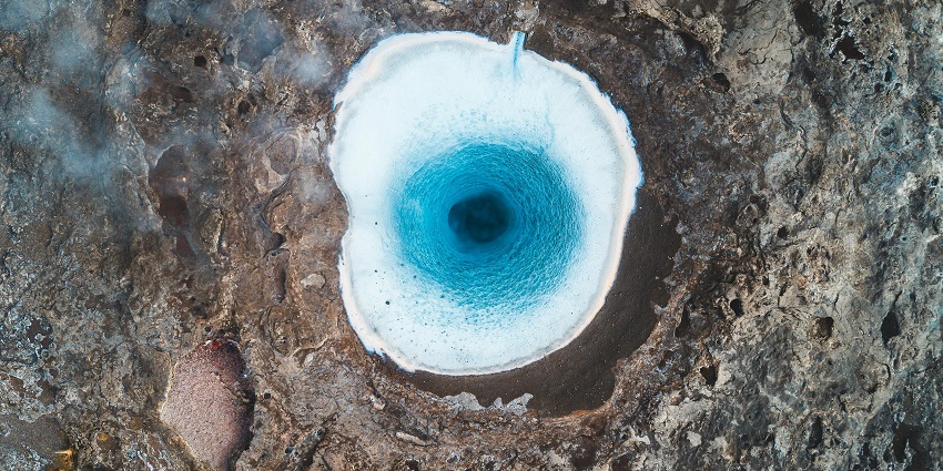 An image showing a prominent rock emerging from the steaming waters of a natural hot spring.