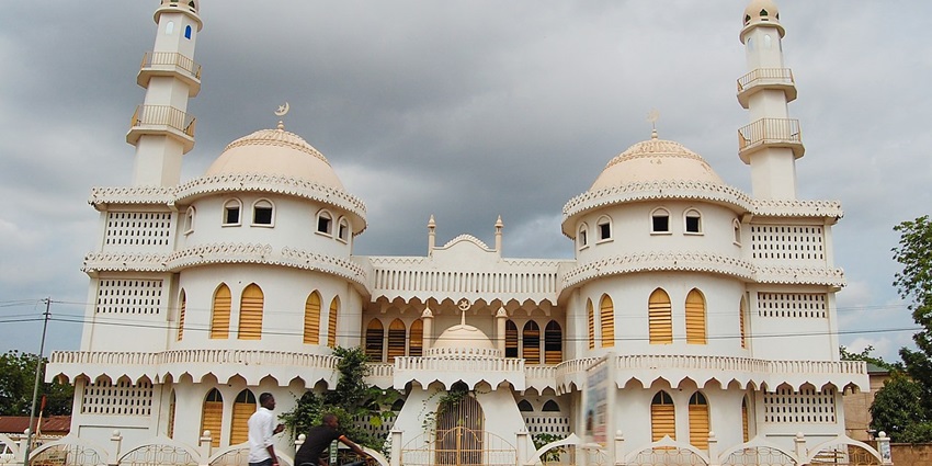 People sitting on their knees preparing for prayer in a mosque with old architecture.