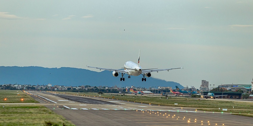 Airplane landing on a runway at an airport under a cloudy sky, viewed from a distance.