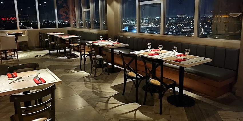 A rooftop bar with glasses and cutlery served on red table napkins and big windows