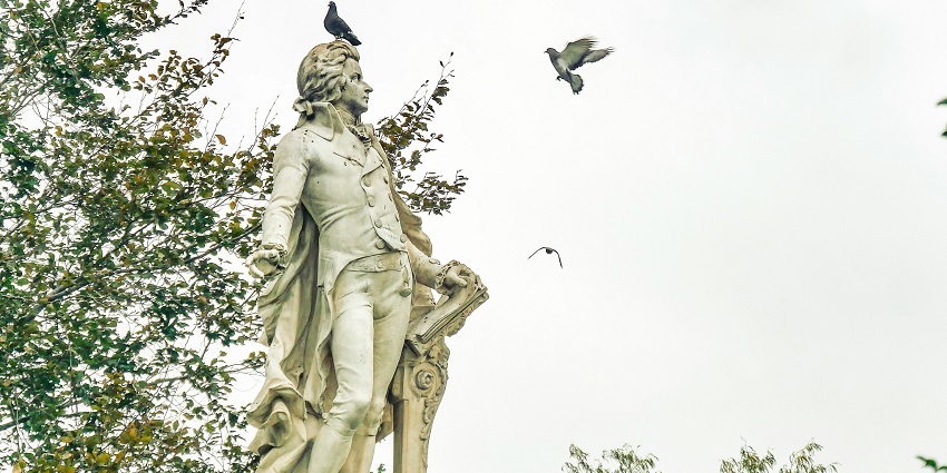 An image of lush greenery and blooming flowers in Burggarten with a statue of Mozart.