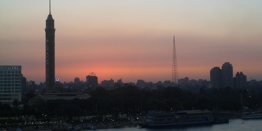 The tall tower of Cairo and other city buildings and the orange sky during the sunset.