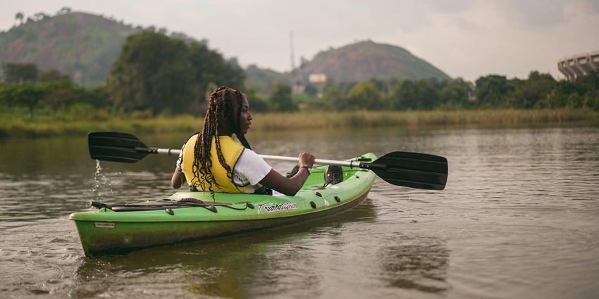 A woman riding and rowing kayak on a lake with hills and green trees in the background.