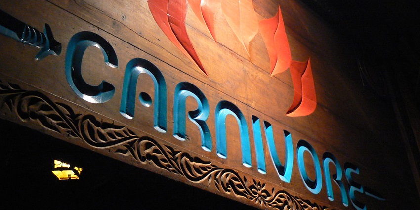 Carnivore signage in blue and an orange flame with a design carved on a wooden wall