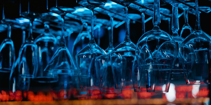 Empty glass wines with a hint of blue hanging upside down and red lights in the back