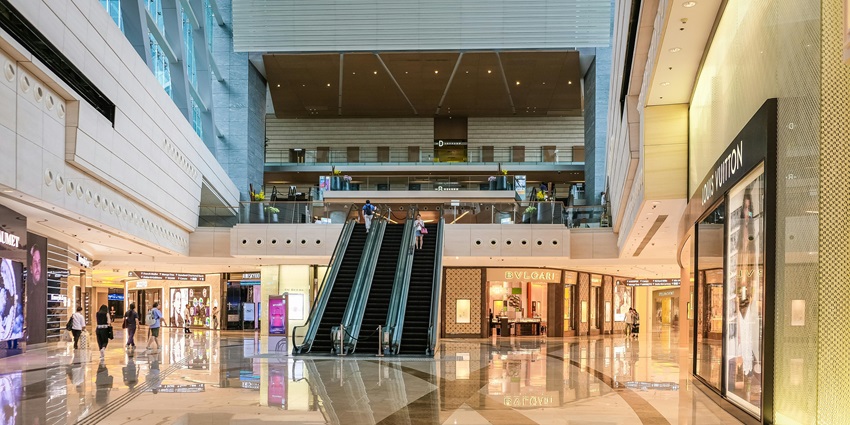 Inside a shopping mall with people and elevators and a Louis Vitton store on the right.