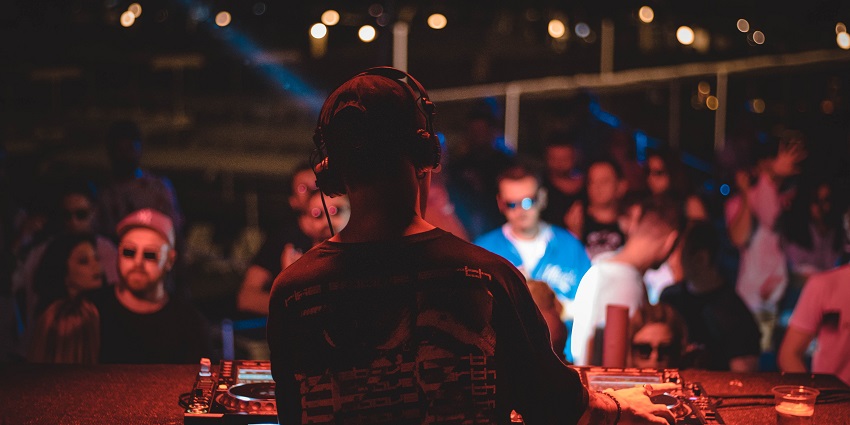 Back of a DJ playing a set while wearing headphones and people standing and enjoying