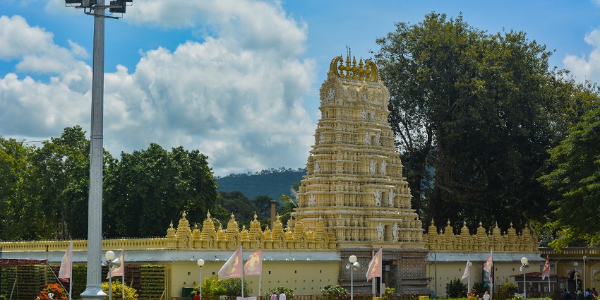 A woman wraps a garland on her wrist in front of Chamundeshwari Temple, as suggested by Mysore travel guide.