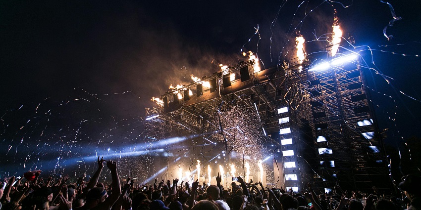 The image shows a lively concert crowd at New Night, with stage lights and fireworks