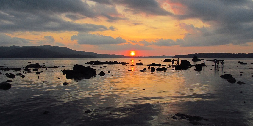 People enjoy near submerged rocks on Chidiya Tapu as the sunsets in the background