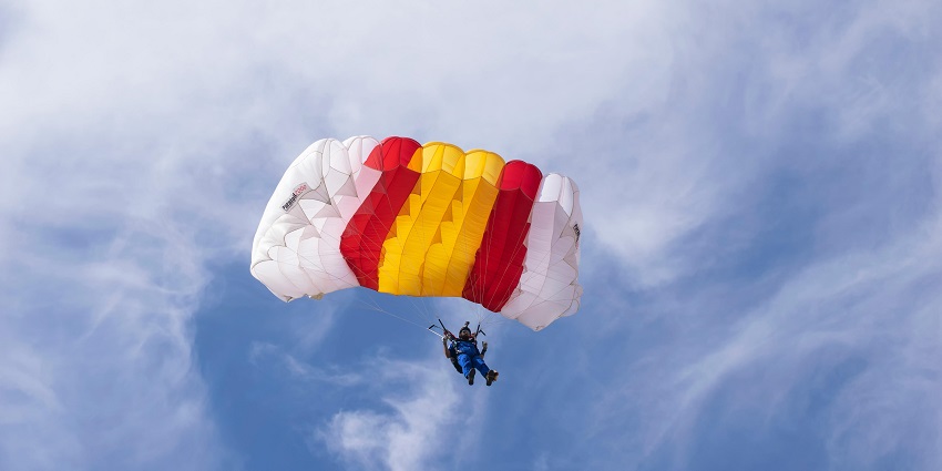 An image of a person descending slowly in a red parachute skydiving in Prague.