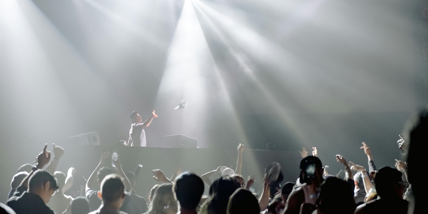 People in a club dancing while raising their hands in the air with vibrant, bright lights.