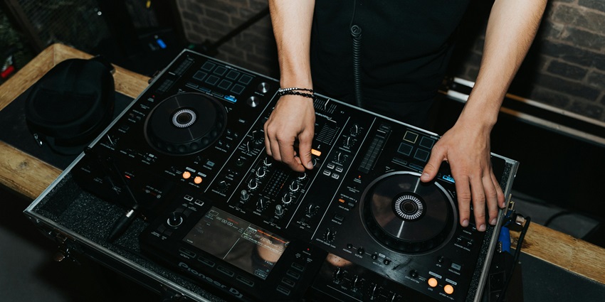 DJ playing songs with the help of his gears and music mixer on the wooden table