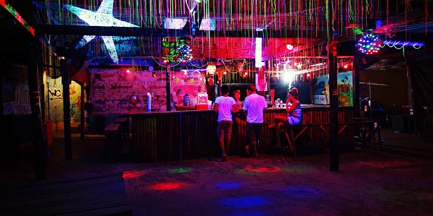 A stylish bar illuminated with vibrant neon lights featuring a sleek counter and a variety of bottles.
