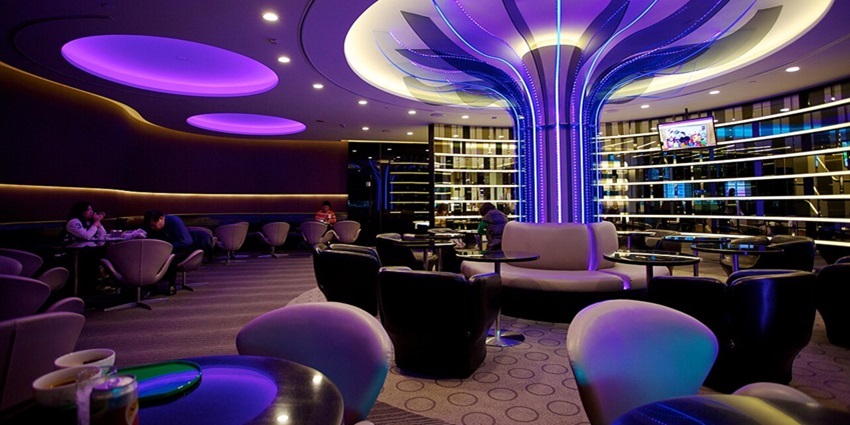 Inside a lounge with blue lights and few people sitting and more empty chairs and tables.
