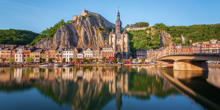 Scenic view of Dinant with river Meuse, cliffside citadel, and Collegiate Church of Notre Dame.