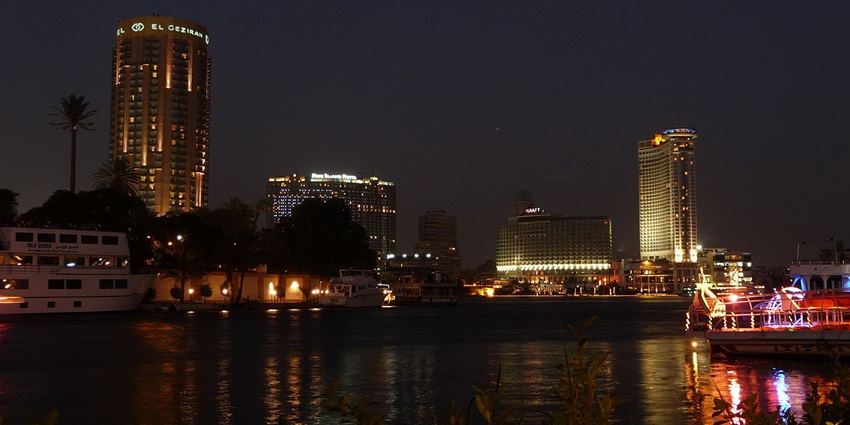 River shore with buildings and colourfully lit boats cruising on the Nile in Cairo