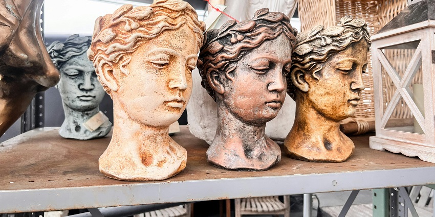 Unfinished sculpted busts of a prominent figure’s face in different colors placed inside a workshop.
