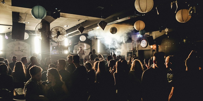 A crowd dancing in a blue-lit enclosure, enjoying the energetic music and vibrant atmosphere.