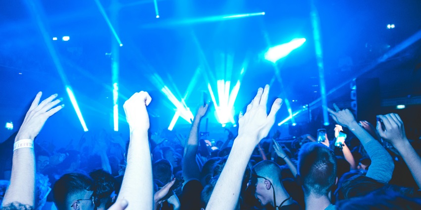 Crowd dancing while raising their hands at the nightclub under bright blue lighting