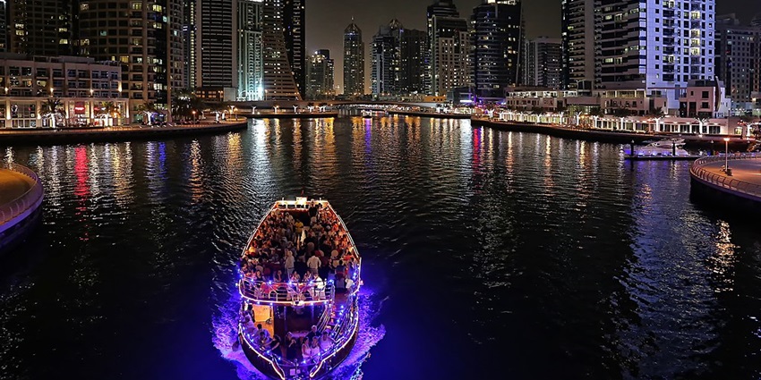 A group of tourists enjoy a nighttime cruise through the Dubai Marina, as suggested by this Dubai travel guide.