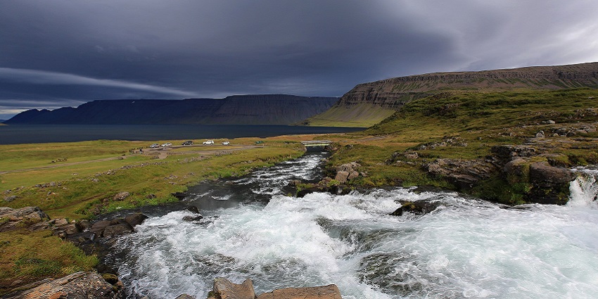 An Image of the water flowing from the Dynjandi Waterfall, with mountain cliffs in the background.