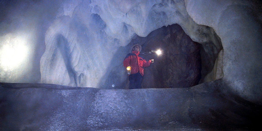 An image of a vast ice cave with frozen waterfalls and crystal formations illuminated inside.